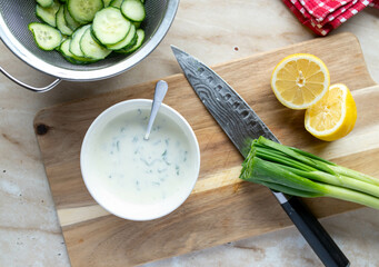 Cucumber salad, making, preparation, ingredients salad sauce on wooden cutting board with knife