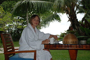Woman in robe is having breakfast in tropical palm garden.