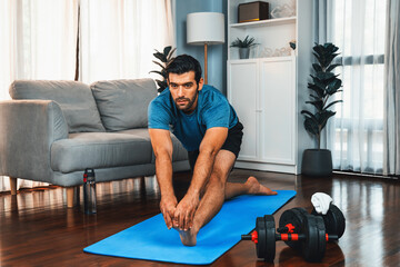Athletic and sporty man doing warmup and stretching before home body workout exercise session for...
