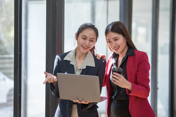 Two women in business attire are looking at a laptop computer