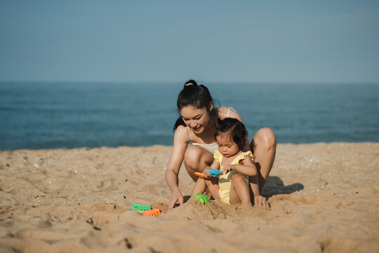 happy toddler baby girl playing sand toy with mother on the sea beach - Powered by Adobe
