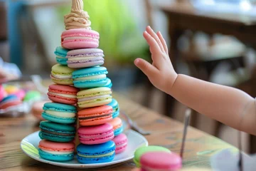  child at a table with a colorful macaron tower, reaching out © primopiano