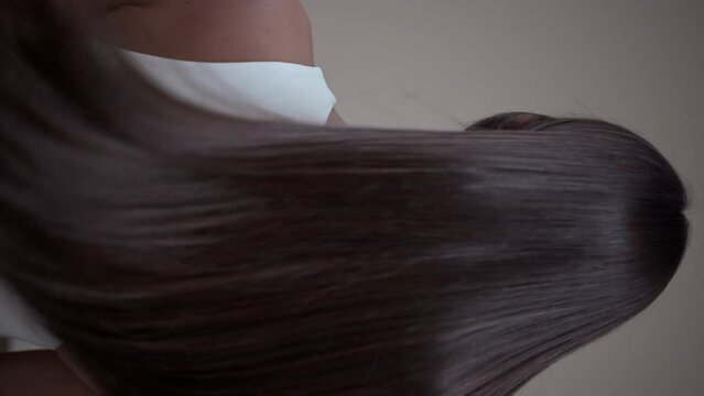 Brunette girl with long straight hair, rear view in the studio on a light background. Vertical video.