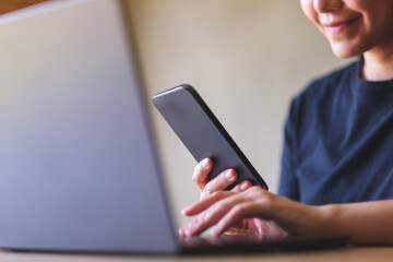Closeup image of a young woman using smart phone and laptop computer