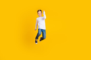 Fototapeta na wymiar Full length photo of lucky impressed boy wear white shirt jumping high rising fists empty space isolated yellow color background