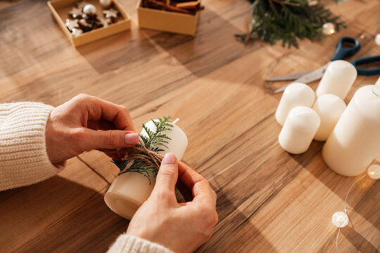 Creating decor for the holidays. Close-up of a girl's hands decorating candles with a fresh thuja branch for Christmas or New Year