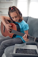 Fototapeta premium Kid playing guitar and watching video lessons on a laptop.