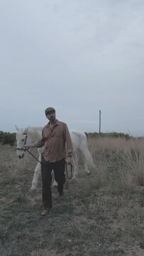 A Spanish cattleman in a beret leads his horse to pasture at sunset. Horse and man walk forward. Slow motion. Vertical video.