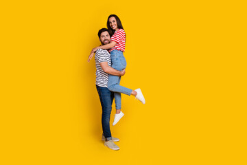 Fototapeta premium Full size photo of couple dressed striped t-shirt cuddle together man hold his girlfriend on arms isolated on yellow color background