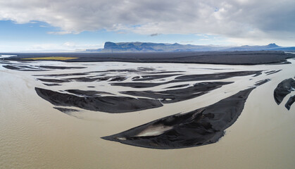 A braiding glacial river creates graphical patterns in volcanic debris on the vast glacial outwash plain Skeiðarársandur in front of the terminus of the Vatnajökull glacier - obrazy, fototapety, plakaty