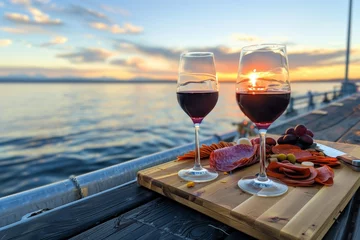 Tuinposter wine glasses on pier with charcuterie board, sunset view © stickerside