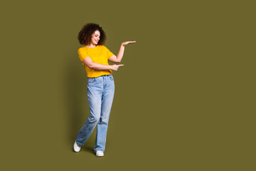 Full length body photo of cheerful girl in yellow t shirt and jeans direct finger low height object isolated on khaki color background