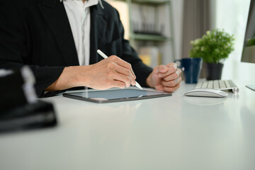 Close up male economist in black suit using digital tablet on white office desk