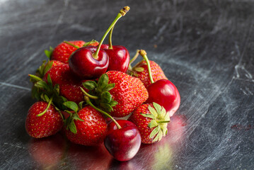 A view of several varieties of fruit and berries scattered on a silver surface, featuring strawberry and cherry.