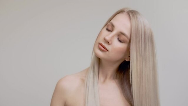 A blonde girl combs her chic long straight hair in the studio on a light background.