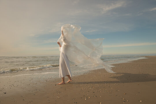 woman in white dress dancing on the beach with thin plastic foil in the wind