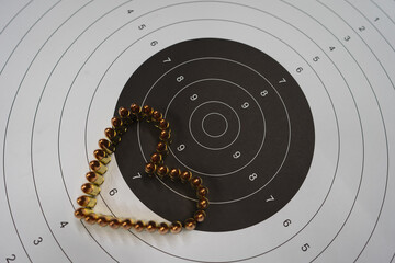 A paper shooting target with a black central circle and a heart made of 9mm cartridges.