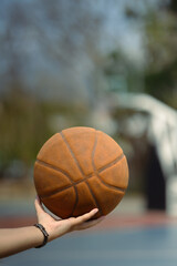 Close up of basketball player holding a ball on an outdoor court. People, sport and active lifestyle concept