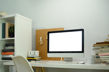 Workplace with blank computer screen and pile of book on white desk