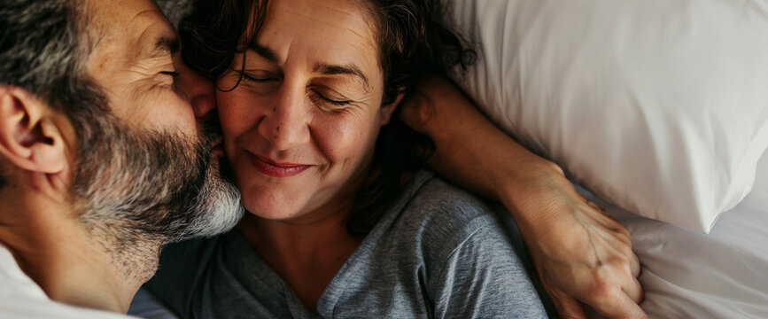 Mature middle aged couple cuddling and kissing in bed, overhead view - Powered by Adobe