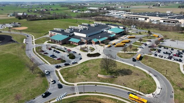 Drone flight over american school with parking yellow buses and traffic on roundabout. High School during sunny day in rural scenic area. Aerial descending top down shot.