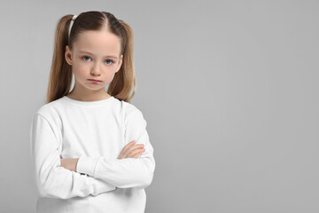 Portrait of sad girl with crossed arms on light grey background, space for text