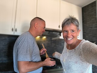 Happy couple cooking together. Husband and wife in their kitchen at home preparing healthy food.Couple in love preparing meal together in the kitchen.The couple's affinity is measured in the kitchen.	 - obrazy, fototapety, plakaty