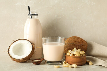 Glass and bottle with alternative milk, coconut and nuts on beige background