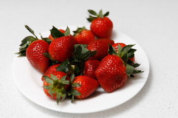 Juicy red strawberries lie on a white saucer