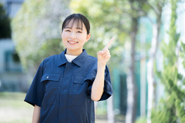 新緑の青空の屋外で作業着を着た女性　ポイントの指差しの正面