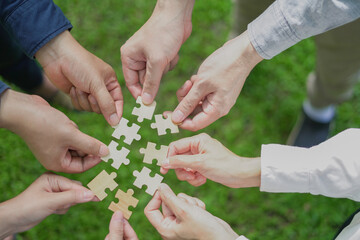 Close-up hand business people of teamwork colleague holding puzzle pieces in a day outdoors on green grass, and jigsaw copy space for your text use. Team Concept. Top view