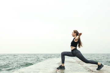 Young woman in sportswear doing sports on the sea pier, space for text