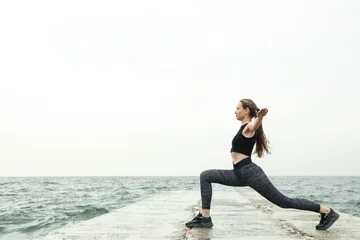 Foto op Plexiglas Young woman in sportswear doing sports on the sea pier, space for text © Atlas