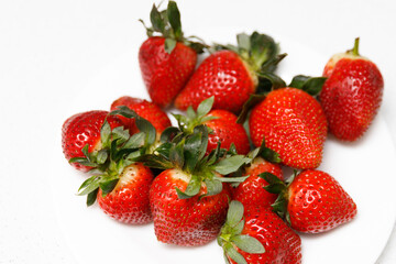 Juicy red strawberries lie on a white saucer