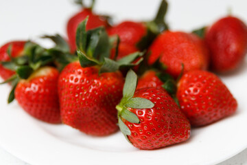 Juicy red strawberries lie on a white saucer