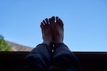 A tranquil scene capturing an adult’s feet silhouetted against a clear blue sky, resting on a...