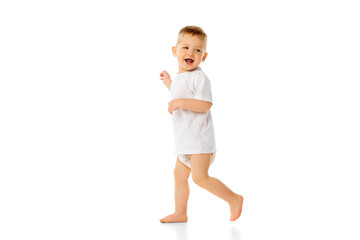 Full-length image of little happy baby boy, child standing in t-shirt and diaper, playing, walking...