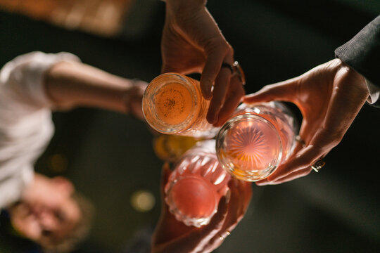 Group of friends celebrate event with alcoholic drinks in pub. People cheer with glasses of cocktails to drink to good luck