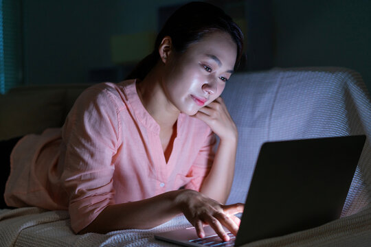 Photo of young Asian woman using laptop in the dark at midnight