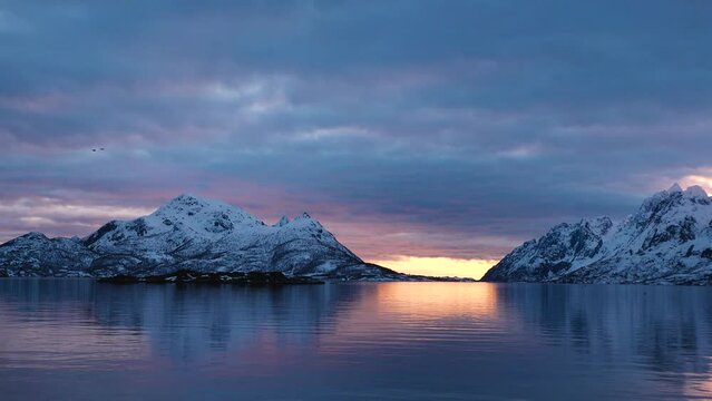 Impressive journeys. Norwegian Fjord Sunset Cruise. Cinematic pink sunset in snowy mountain. Scenic view of Norwegian arctic sea surrounded by fjord covered with snow, ice. Travel concept.