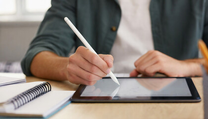 Boy student sitting at a desk using a tablet or iPad with a white stylus pen studying doing homework.