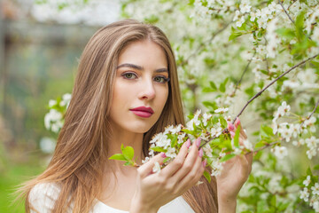 Fototapeta premium Fashion portrait of young woman with natural makeup and healthy long brown hair in blossom park outdoors. Natural female beauty