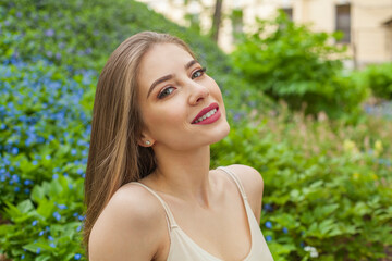 Happy young woman with natural makeup and healthy long brown hair in blossom park outdoors. Natural female beauty portrait