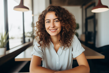 a woman with curly hair is sitting at a table with her arms crossed and smiling
