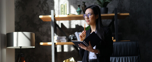 An Asian executive businesswoman focuses on her work in her modern office, embodying...