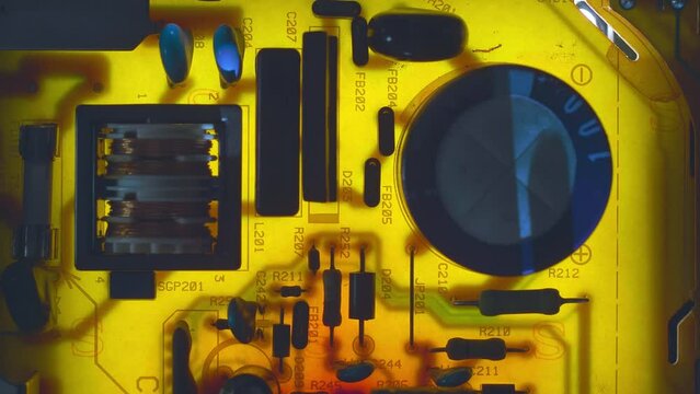 A printed circuit board with capacitors, a transformer and other radio components that cast shadows that move in the wake of the light source. Closeup. Macro