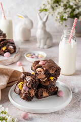 Chocolate brownie with Easter candies in the form of colored eggs with a bottle of milk. Easter dessert. Copy space.