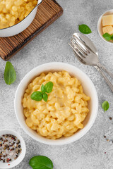 Mac and cheese in a white bowl with fresh basil on top on a gray concrete background. American cuisine, comfort food. Copy space.