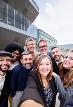 Vertical image of a cheerful group of multiracial business people taking a selfie together outside office building, looking at the camera smiling. Copy space.