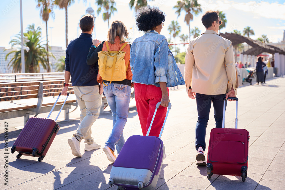 Wall mural back view of a group of unrecognizable people walking with their luggage for the street city carefre